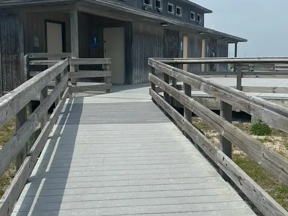 Railed wooden ramp leading to a weathered-shingle beach access bathhouse