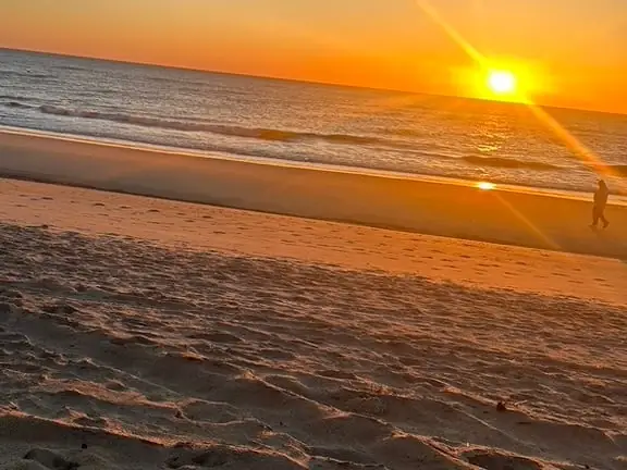 Sun rising over the Atlantic as a lone walker crosses the wet sand
