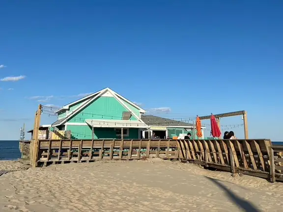 Aqua-painted oceanfront bar behind a wooden deck on the sand under a blue sky